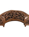 Brown wood arch sculpture with hand-carved animal and floral motifs on a dark antique chest.