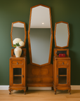 Green vintage vanity table with marble tabletops and octagonal mirrors, styled with a vase and red box against a green wall.