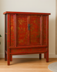 Red lacquer 19th century armoire with gilt décor on light wood floor next to a potted plant.