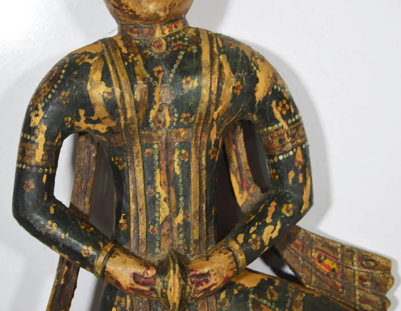Wooden figurine of a seated figure with intricate carvings on a white background
