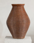 Brown ribbed pottery vase with burnished surface on white pedestal, light gray background, close-up.