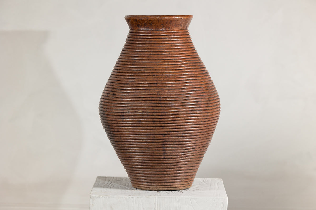 Brown ribbed vintage pottery vase with burnished surface on a white pedestal against a light background.