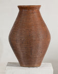 Brown ribbed vintage pottery vase with burnished surface on a white pedestal against a light background.