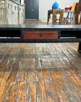 Black lacquer patina carved wood coffee table with red drawer and open shelves on rustic wood floor.