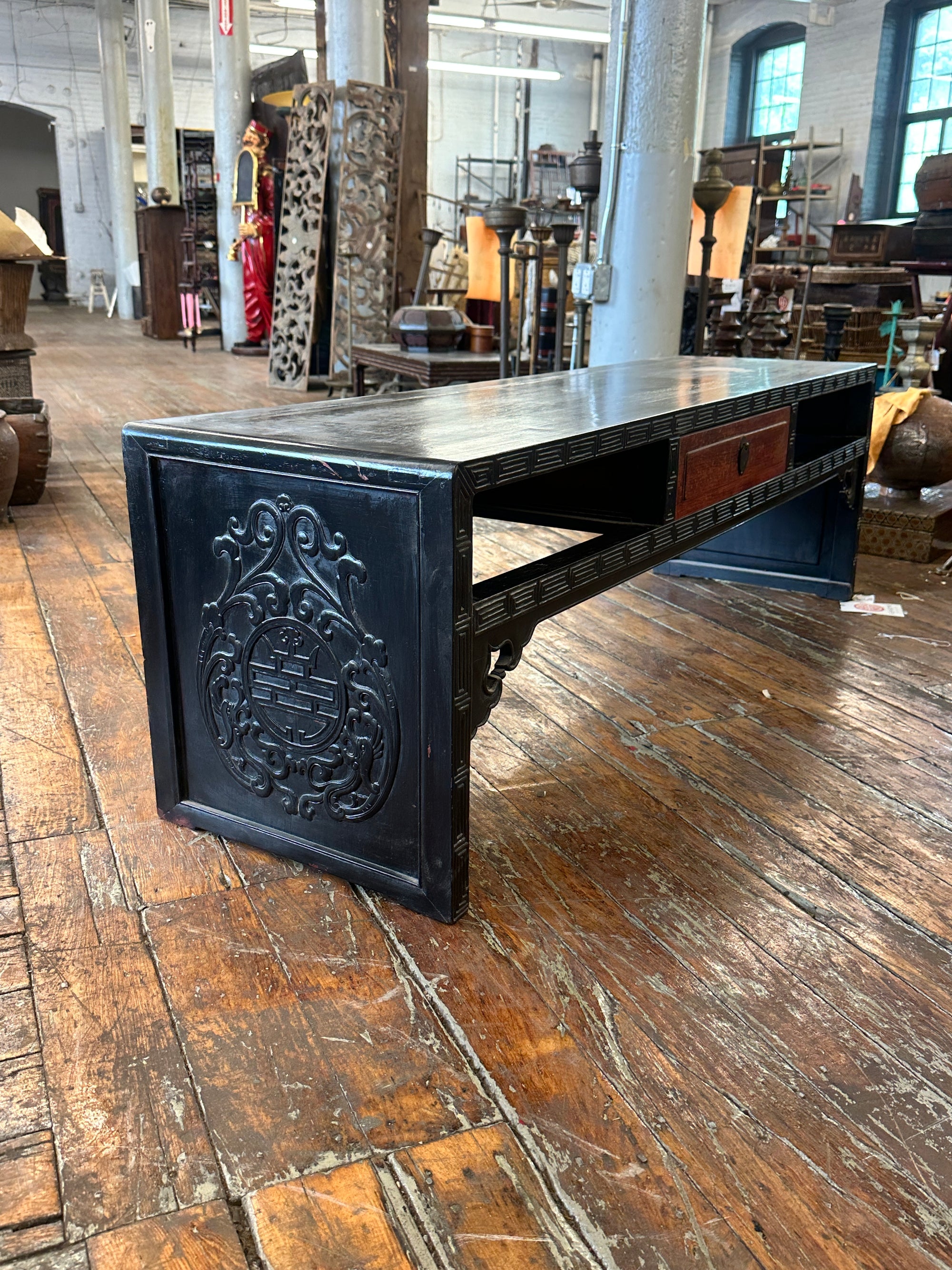 Black lacquer antique Chinese carved coffee table with drawer on rustic wood floor in antique shop setting.