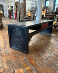 Black lacquer antique Chinese carved coffee table with drawer on rustic wood floor in antique shop setting.