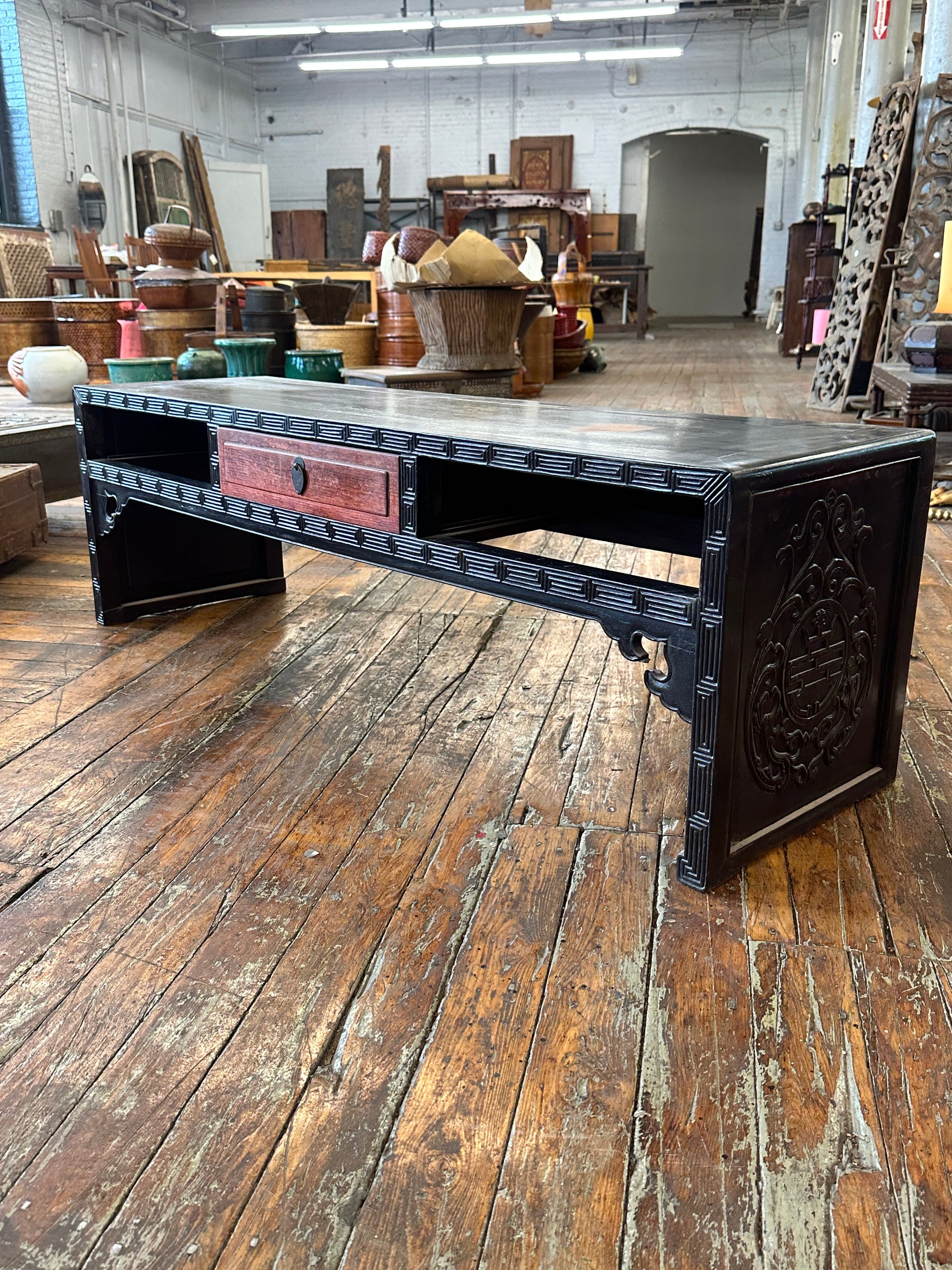 Black wooden bench with red drawer on worn floor next to antique black lacquer Chinese carved coffee table.