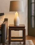 Close-up of ceramic lamp with beige shade on Qing Dynasty brown lacquer low table next to brown sofa with cream pillow.