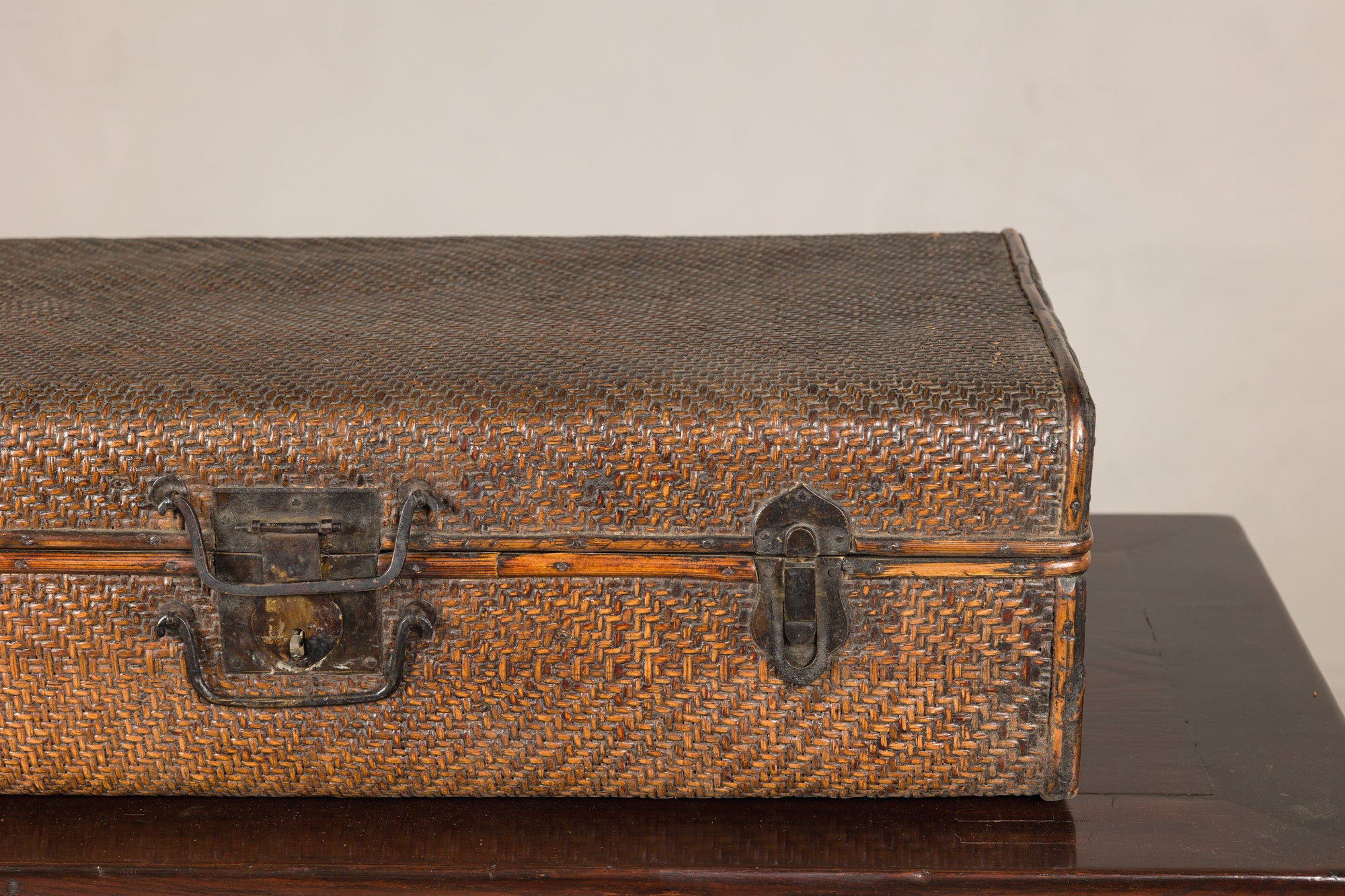 Brown woven rattan suitcase trunk with iron hardware on dark wooden table, Late Qing Dynasty style.