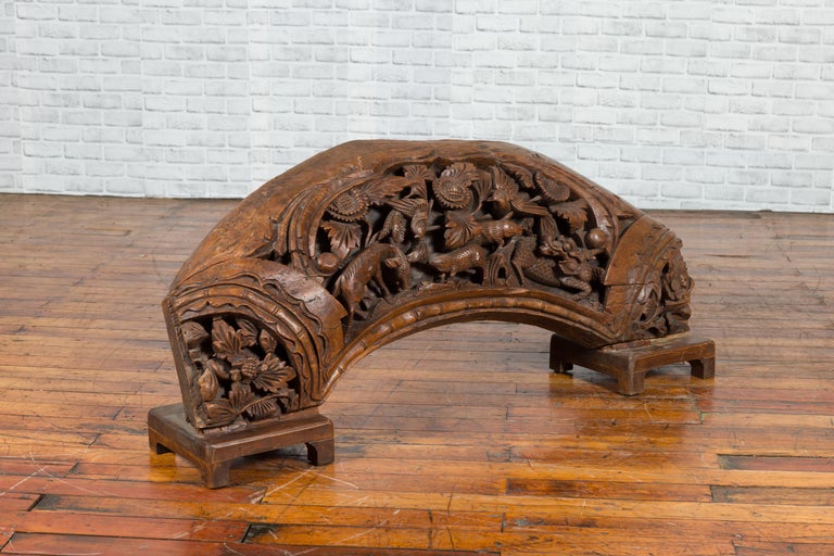 Brown wood arch sculpture with hand-carved animal and floral motifs on a dark antique chest.