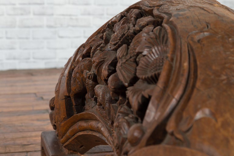 Brown wood arch sculpture with hand-carved animal and floral motifs on a dark antique chest.