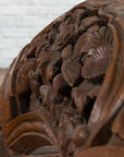 Brown wood arch sculpture with hand-carved animal and floral motifs on a dark antique chest.