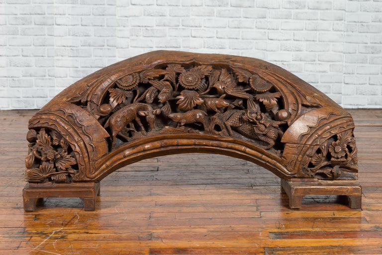 Brown wood arch sculpture with hand-carved animal and floral motifs on a dark antique chest.