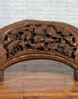 Brown wood arch sculpture with hand-carved animal and floral motifs on a dark antique chest.