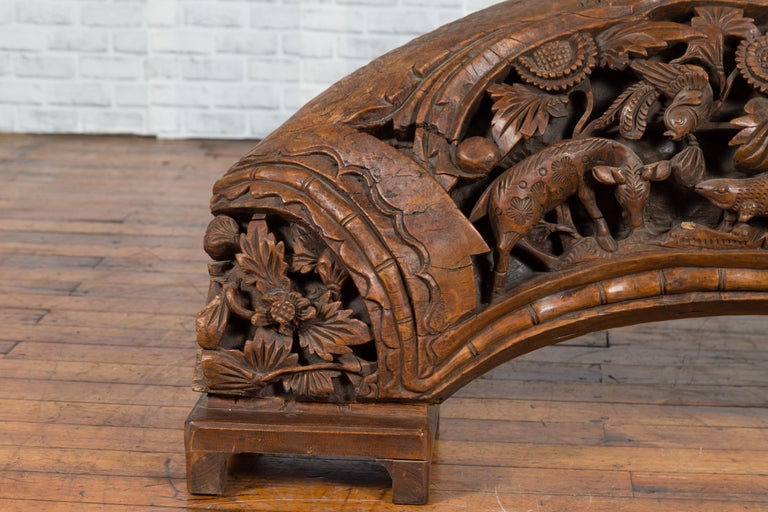Brown wood arch sculpture with hand-carved animal and floral motifs on a dark antique chest.