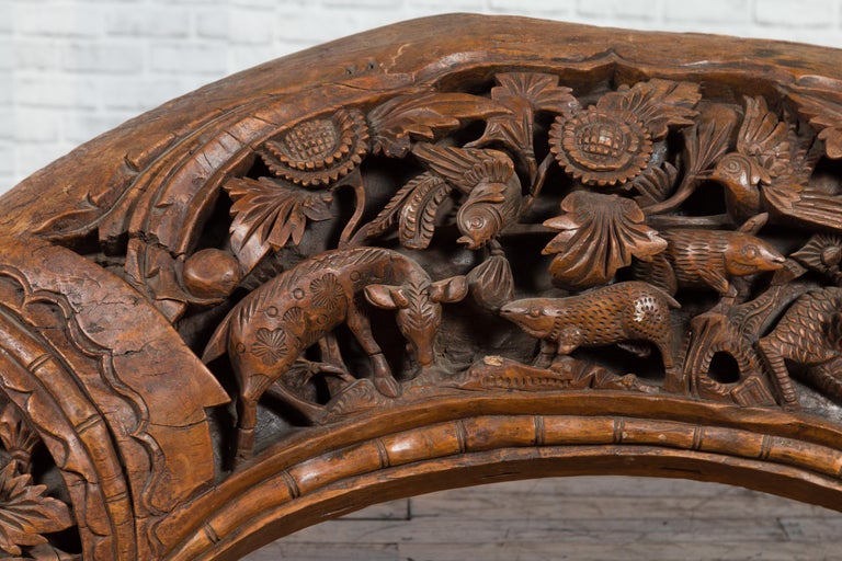 Brown wood arch sculpture with hand-carved animal and floral motifs on a dark antique chest.