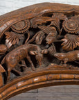 Brown wood arch sculpture with hand-carved animal and floral motifs on a dark antique chest.