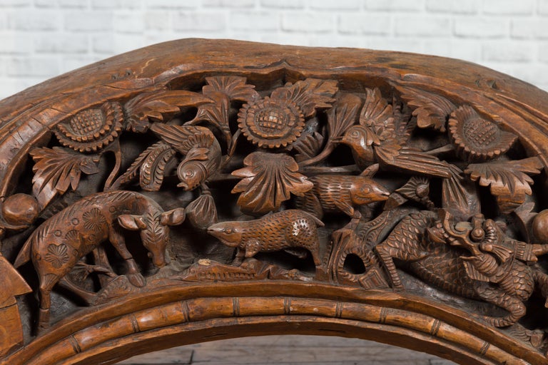 Brown wood arch sculpture with hand-carved animal and floral motifs on a dark antique chest.