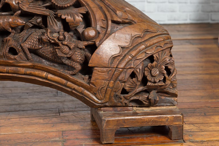 Brown wood arch sculpture with hand-carved animal and floral motifs on a dark antique chest.