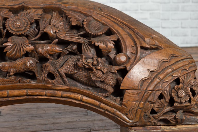 Brown wood arch sculpture with hand-carved animal and floral motifs on a dark antique chest.