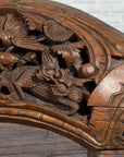 Brown wood arch sculpture with hand-carved animal and floral motifs on a dark antique chest.