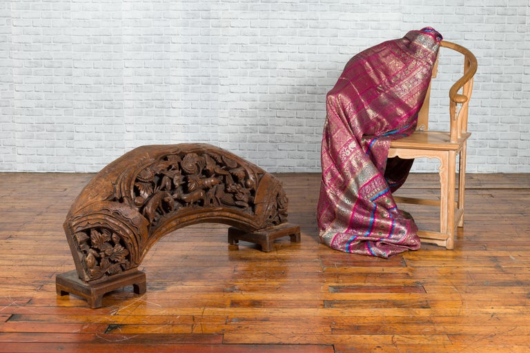 Brown wood arch sculpture with hand-carved animal and floral motifs on a dark antique chest.