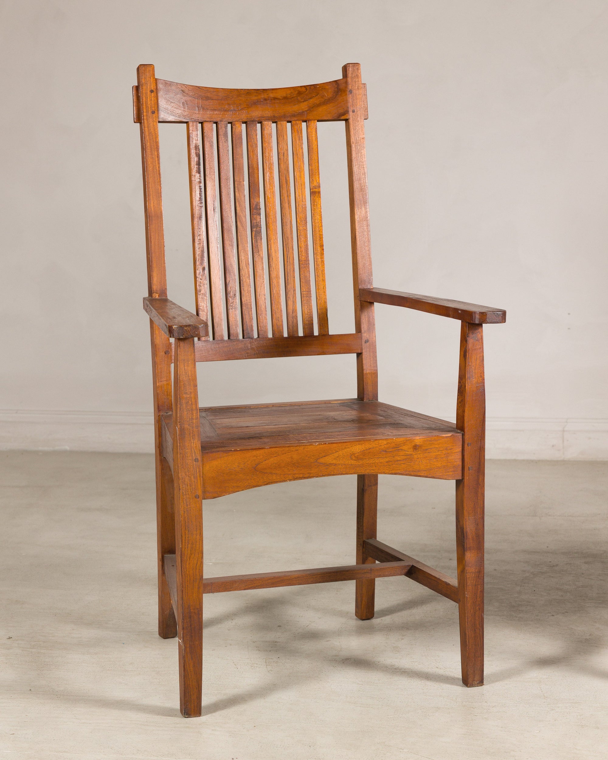 Pair of brown teak Dutch Colonial armchairs with vertical slats on a plain floor, light wall background.
