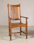 Pair of brown teak Dutch Colonial armchairs with vertical slats on a plain floor, light wall background.