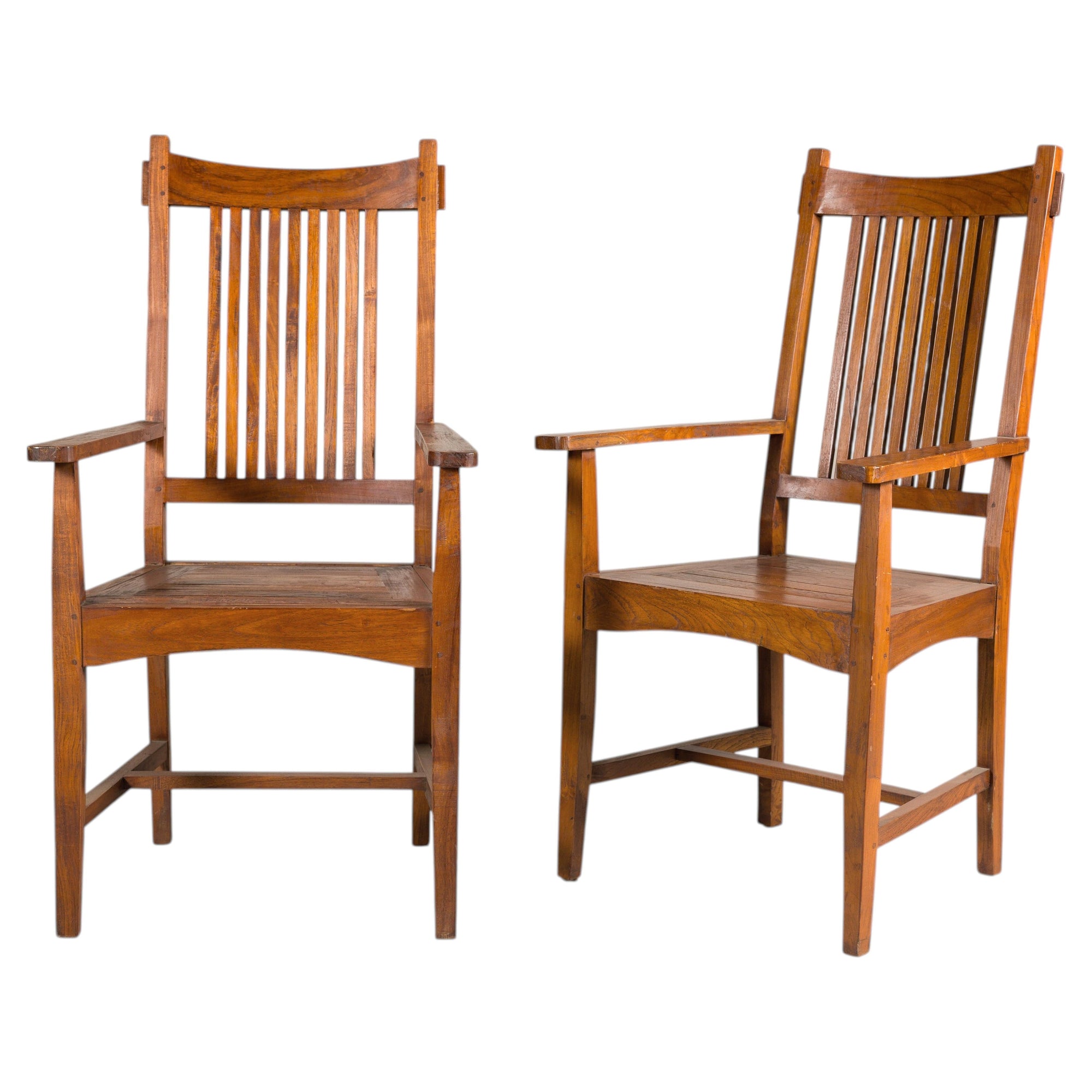 Brown teak wood Dutch colonial dining armchairs with vertical slats, angled on white background.