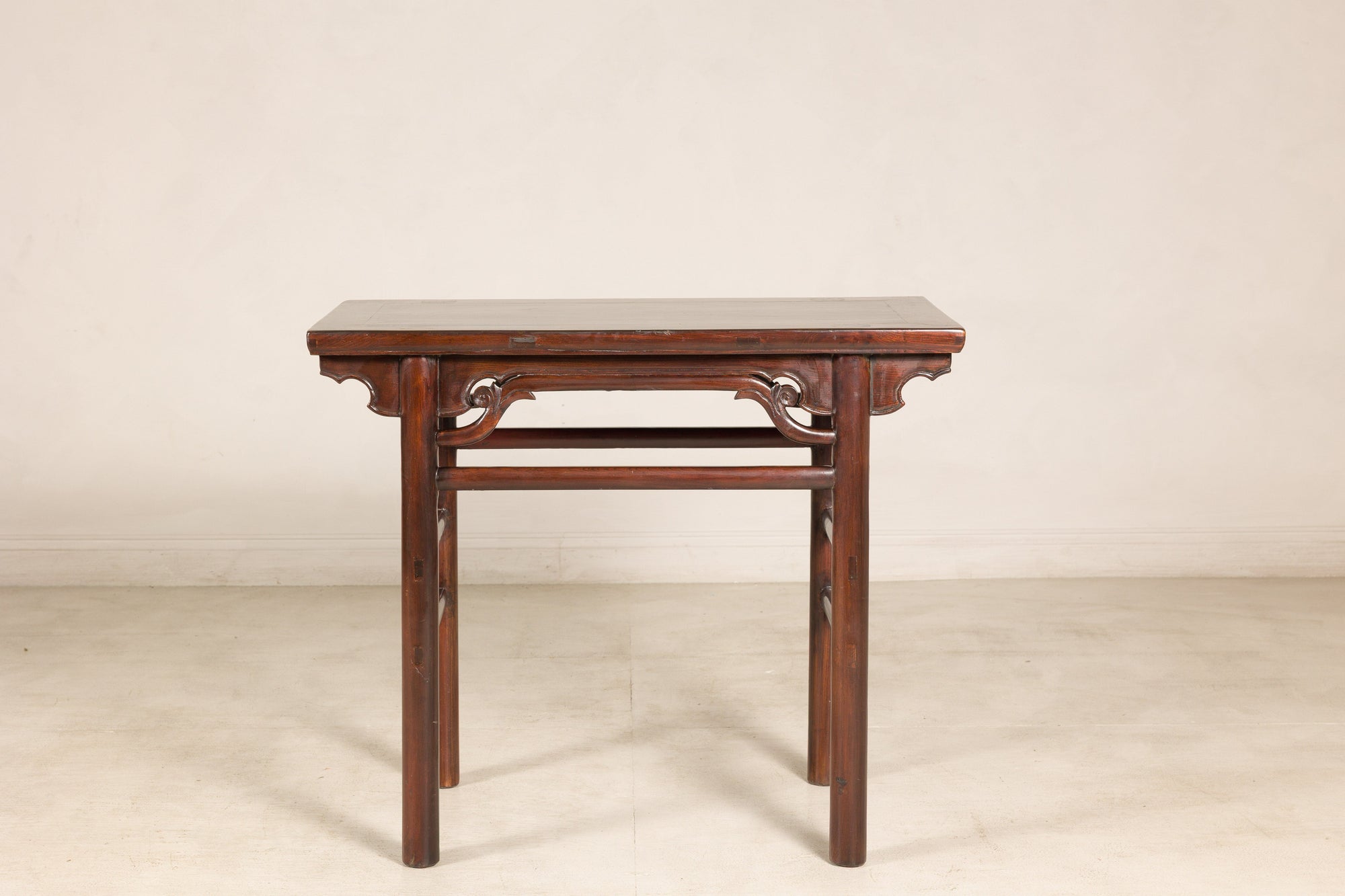 Brown Chinese elm console table with carved spandrels against a plain wall, antique wood furniture detail.