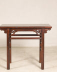 Brown Chinese elm console table with carved spandrels against a plain wall, antique wood furniture detail.