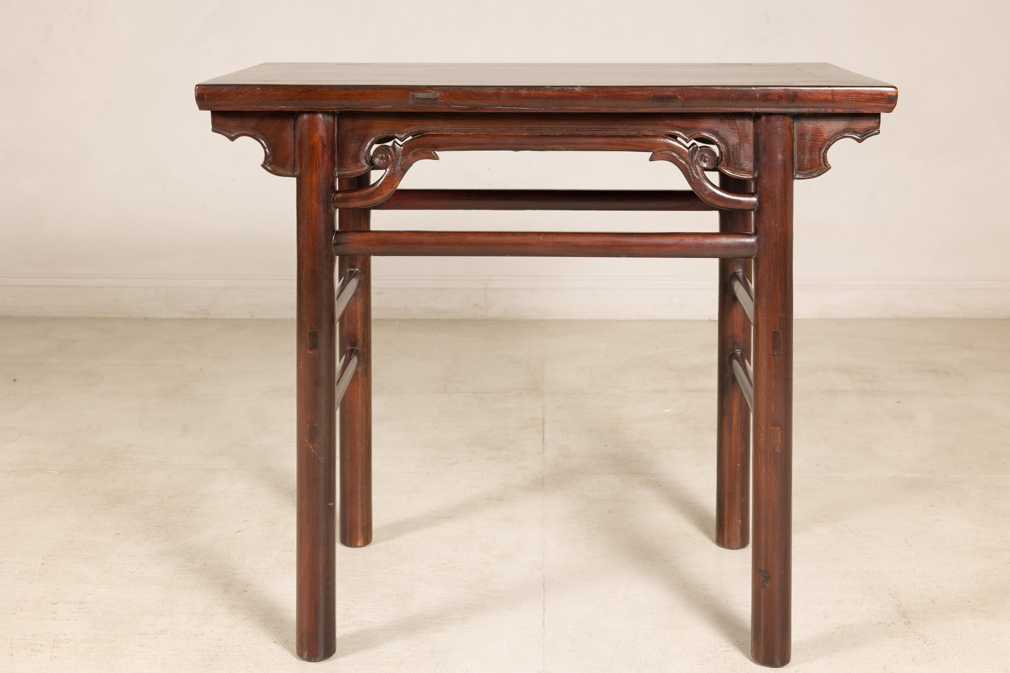 Dark wood Chinese elm console table with carved spandrels and straight legs, Qing dynasty style against plain backdrop.