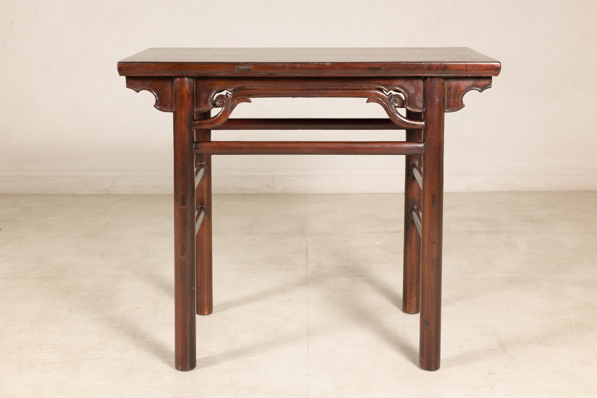 Antique Chinese elm console table with carved spandrels on a light floor against a plain wall.
