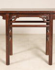 Antique Chinese elm console table with carved spandrels on a light floor against a plain wall.