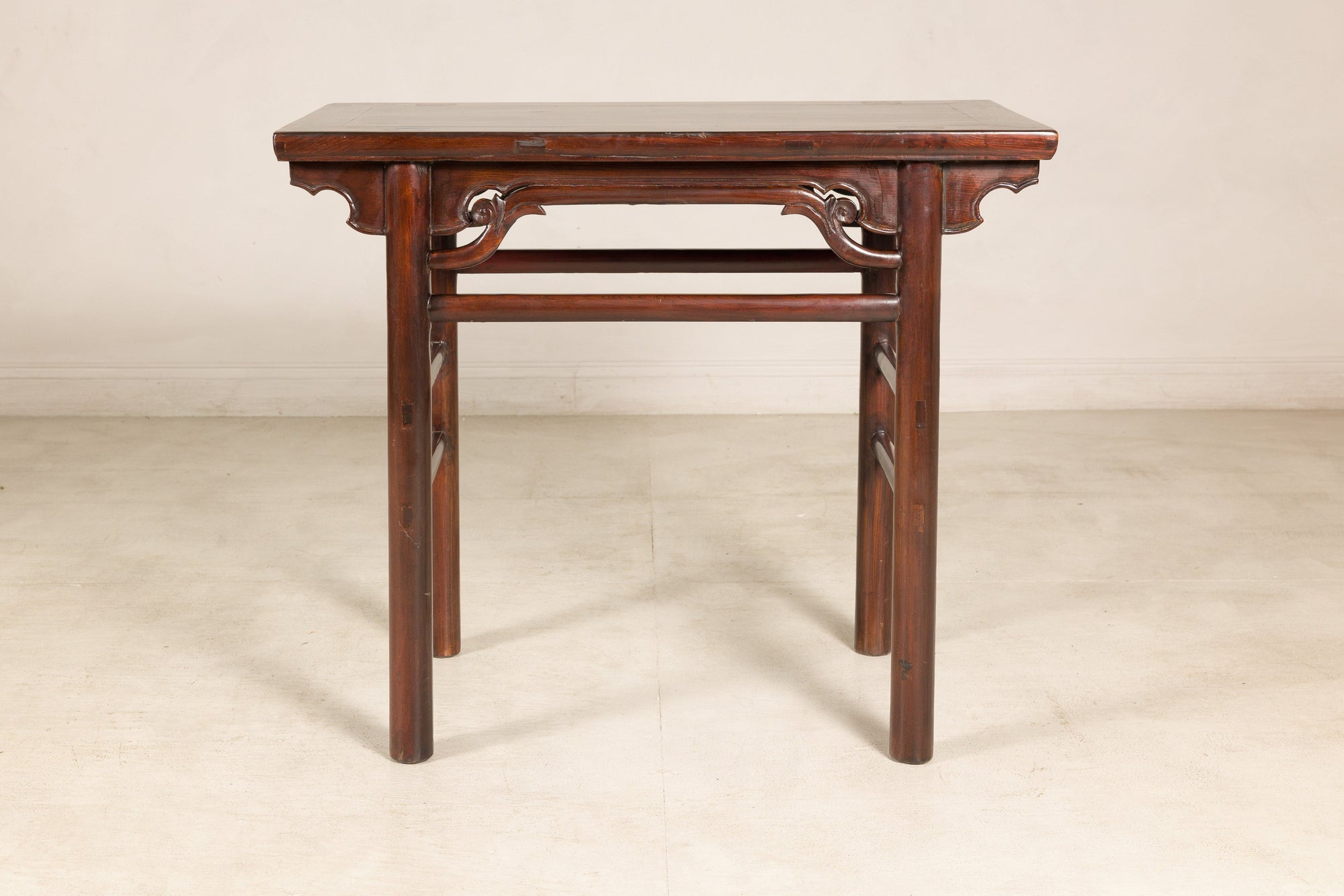 Antique Chinese elm console table with carved spandrels on a light floor against a plain wall.