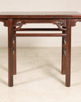 Antique Chinese elm console table with carved spandrels on a light floor against a plain wall.
