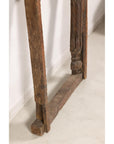 Brown wood hand-carved Indian frame with arched opening on light floor against white wall.