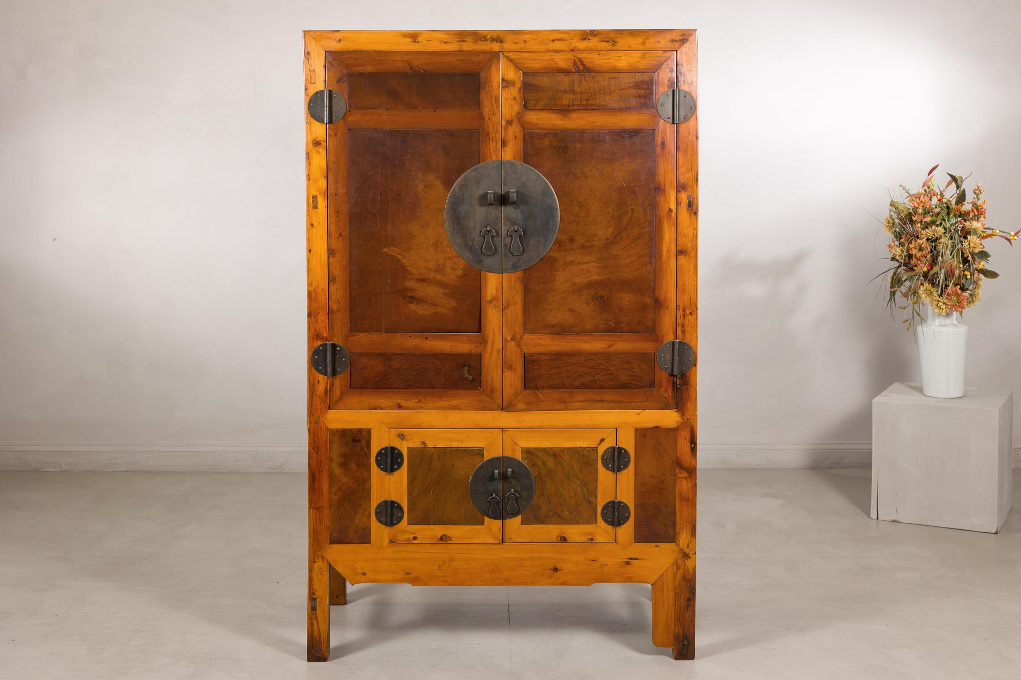 Antique Chinese elm and burl cabinet with brass hardware beside a pedestal with dried flowers.