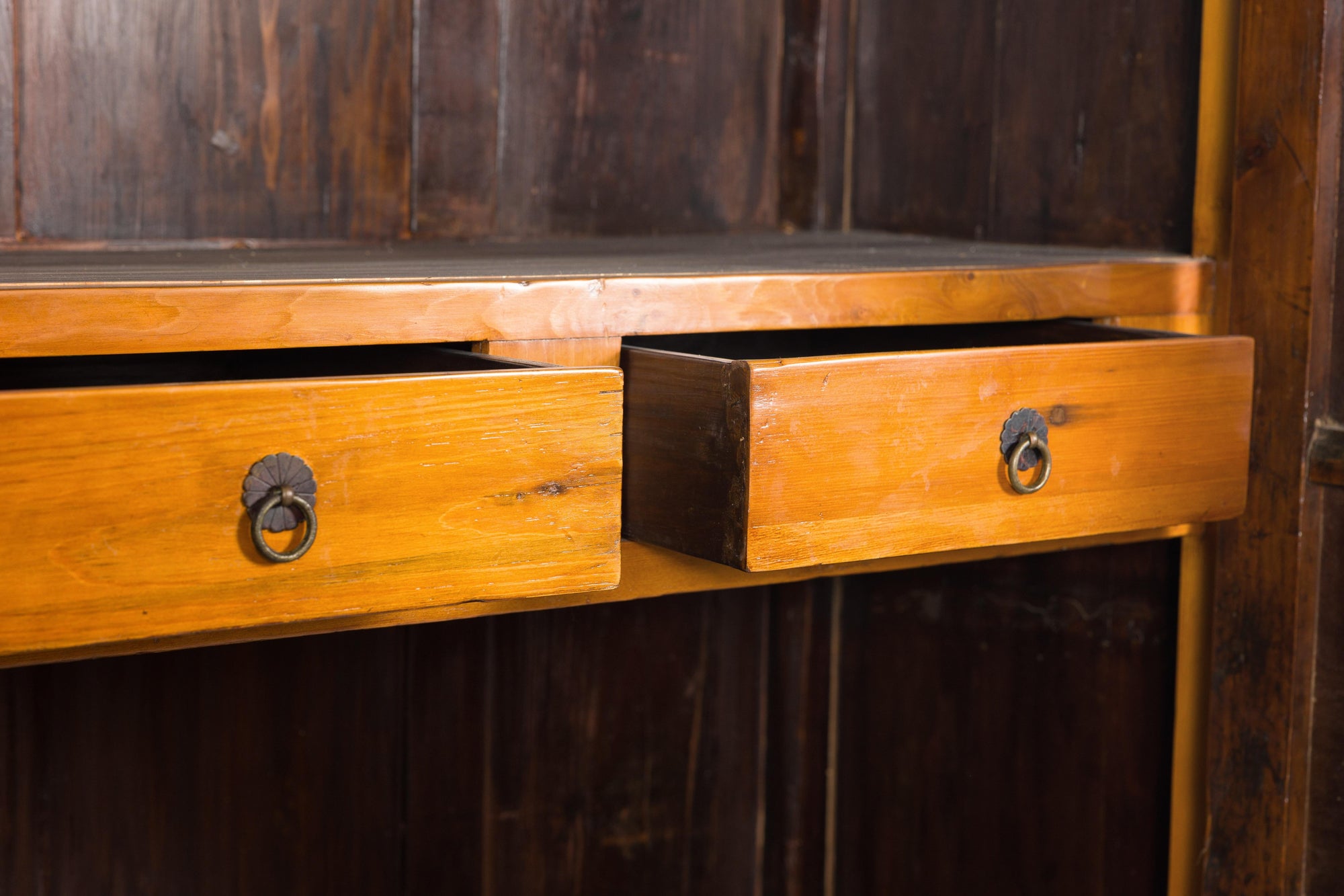 Brown Chinese elm and burl cabinet with brass hardware, two drawers partially open, against dark wood background.