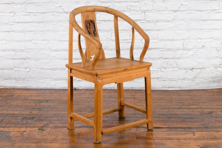 Brown elmwood Qing Dynasty chair with carved medallion, placed on wooden floor against white brick wall backdrop.