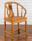 Brown elmwood Qing Dynasty chair with carved medallion, placed on wooden floor against white brick wall backdrop.