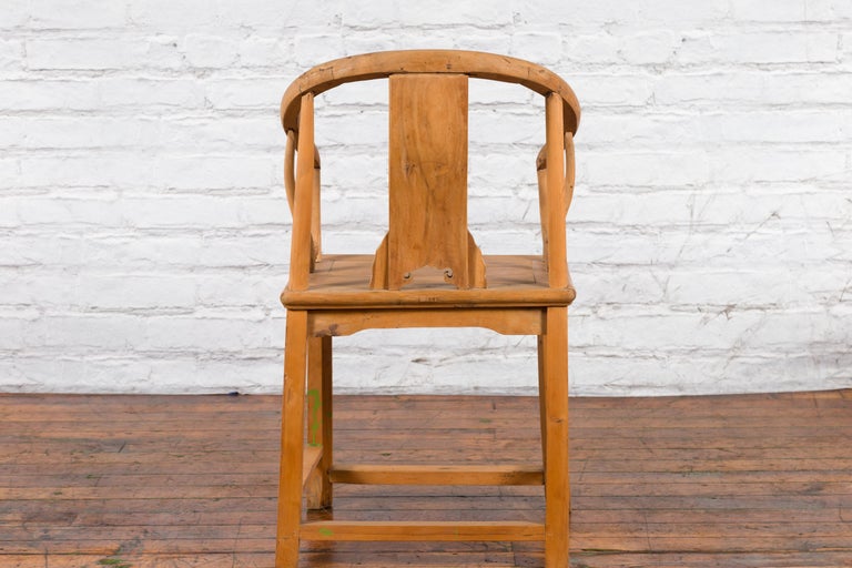 Brown elmwood Chinese Qing Dynasty chair with carved medallion, on wood floor against white brick wall.
