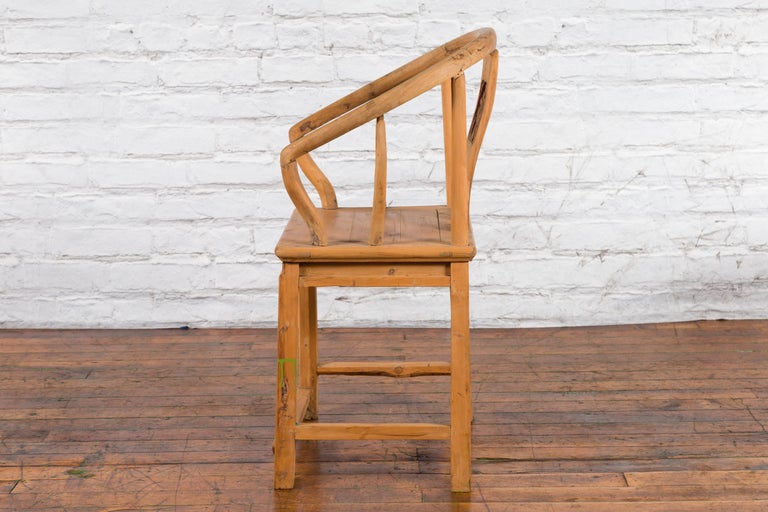 Brown elmwood Qing Dynasty chair with carved medallion, curved backrest and arms on wooden floor by brick wall.