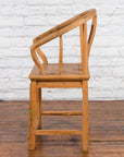 Brown elmwood Qing Dynasty chair with carved medallion, curved backrest and arms on wooden floor by brick wall.