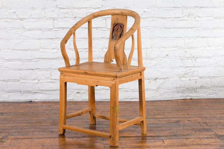 Brown elmwood Qing Dynasty chair with carved medallion, on wood floor against a white brick wall.