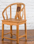 Brown elmwood Qing Dynasty chair with carved medallion, on wood floor against a white brick wall.
