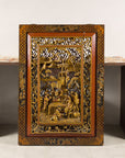 Gold giltwood Qing wall panel with figural court scene, displayed against patterned table and white wall.