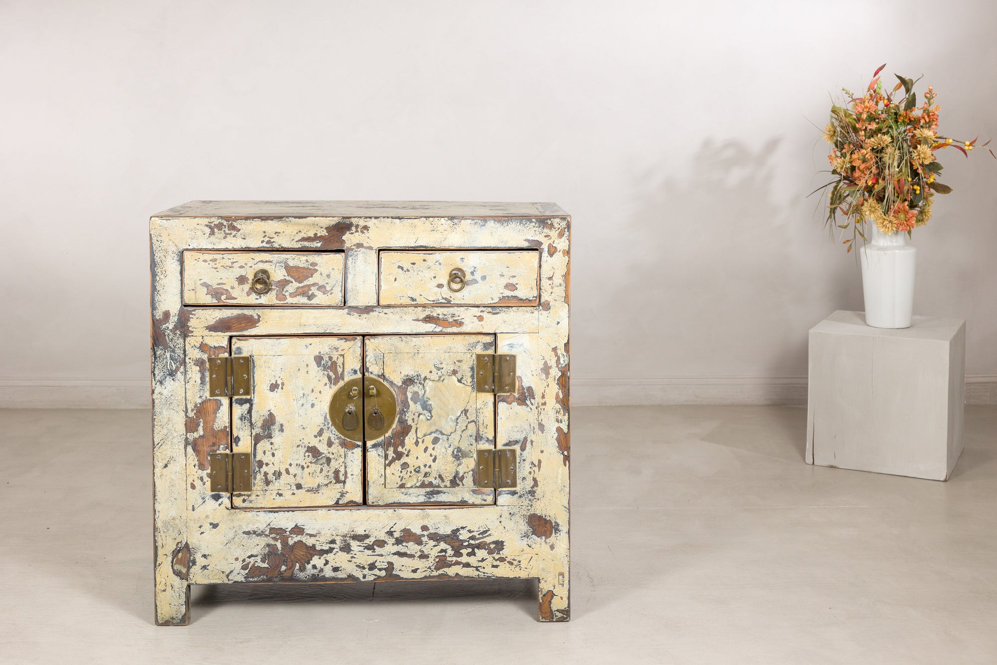 Small distressed cream cabinet displayed beside a floral arrangement