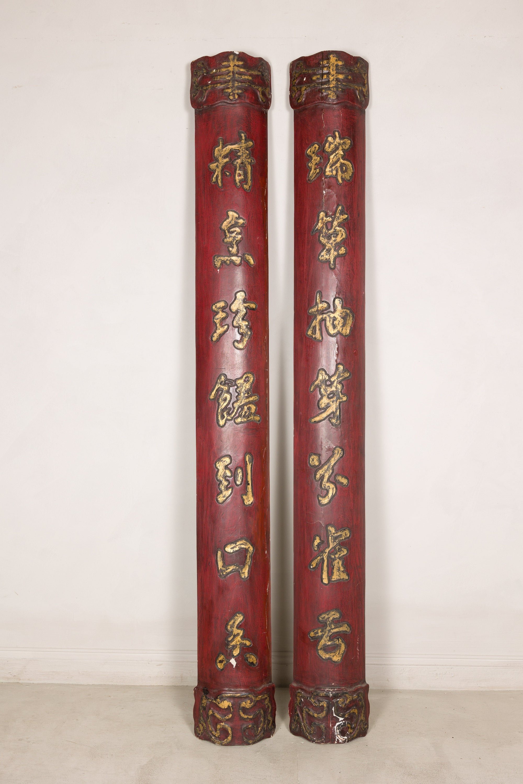 Pair of tall red and gilt Chinese calligraphy panels displayed against a pale wall