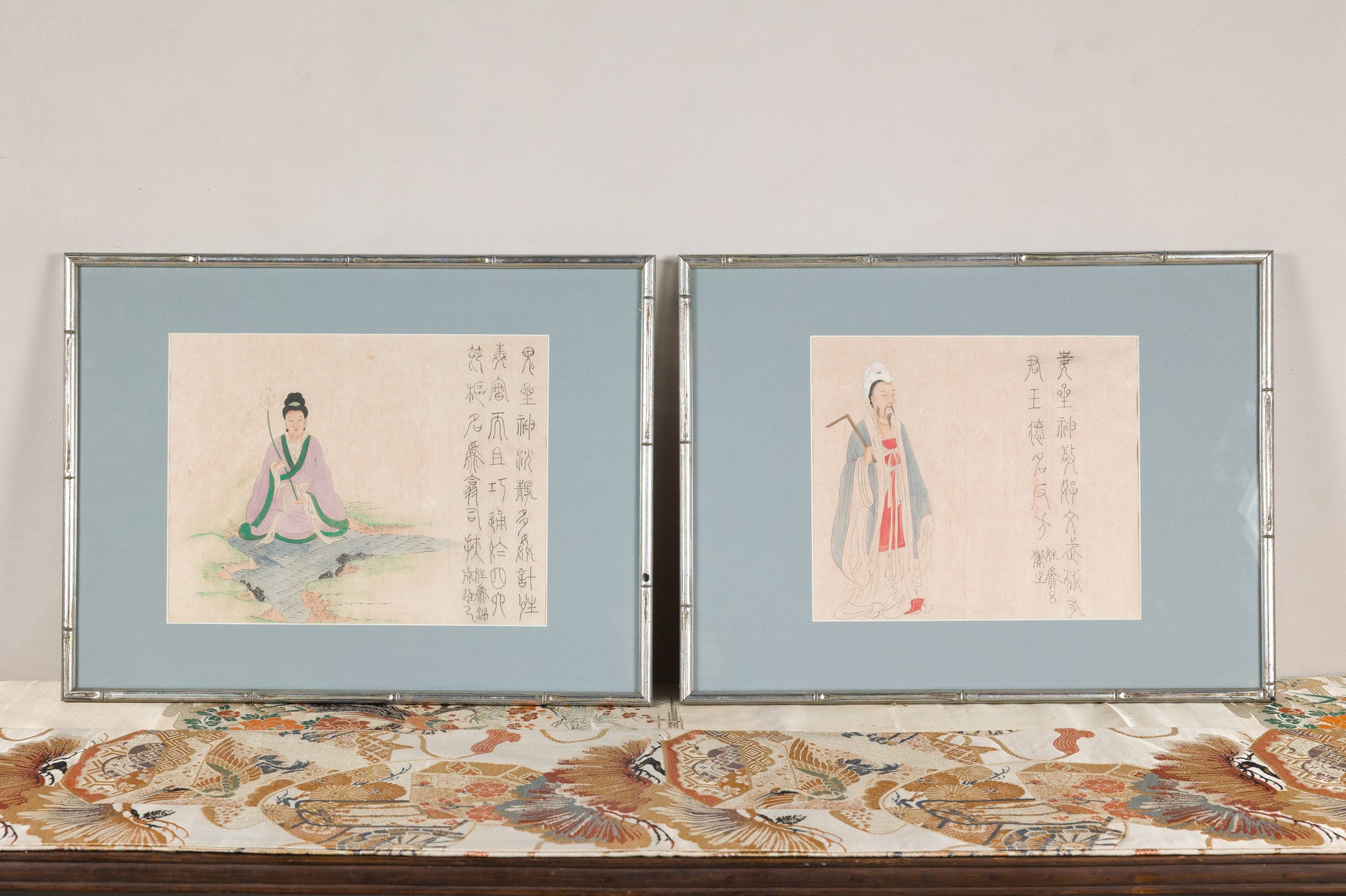 Pair of framed Japanese figural prints displayed on a patterned textile